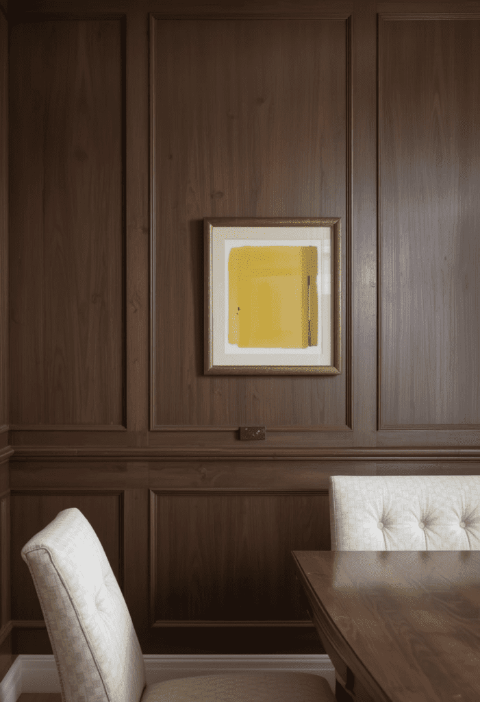 A brown accent wall with wooden paneling, featuring a small framed yellow artwork for contrast.