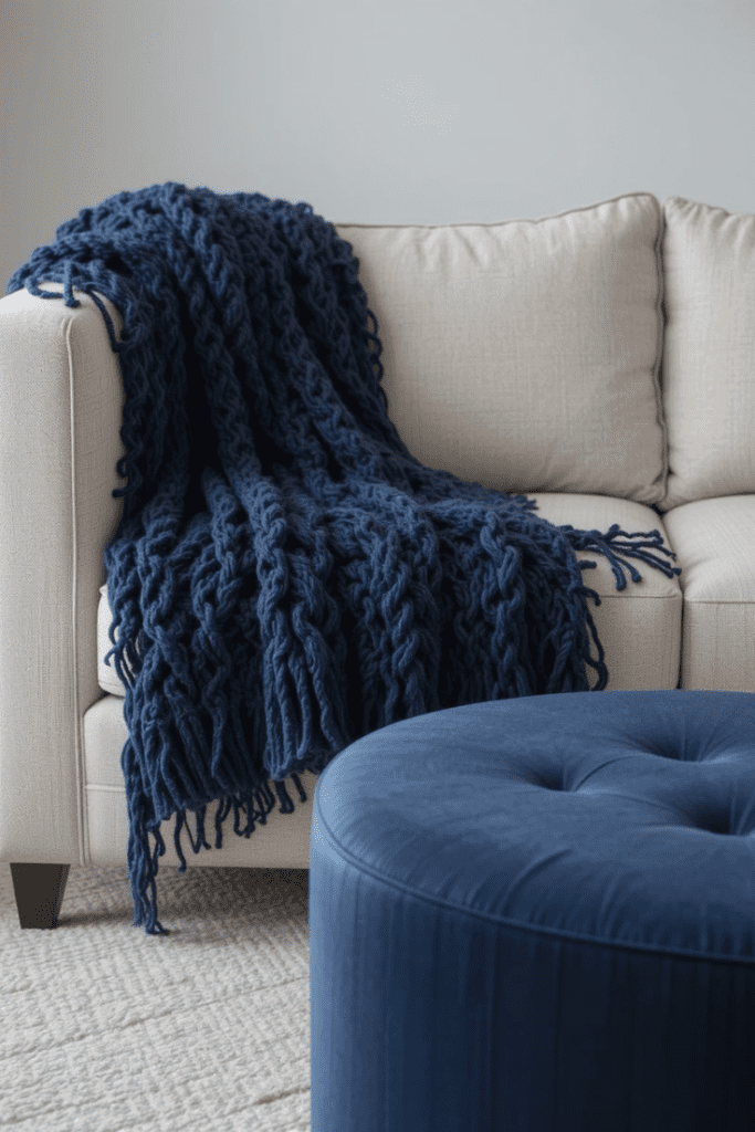 A cozy living room featuring navy blue textiles, including a throw blanket and an ottoman.